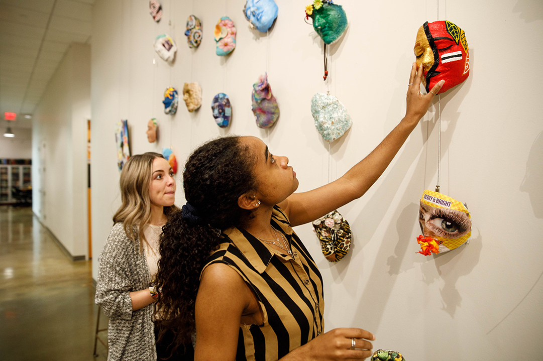 Two young women hanging masks on a gallery wall
