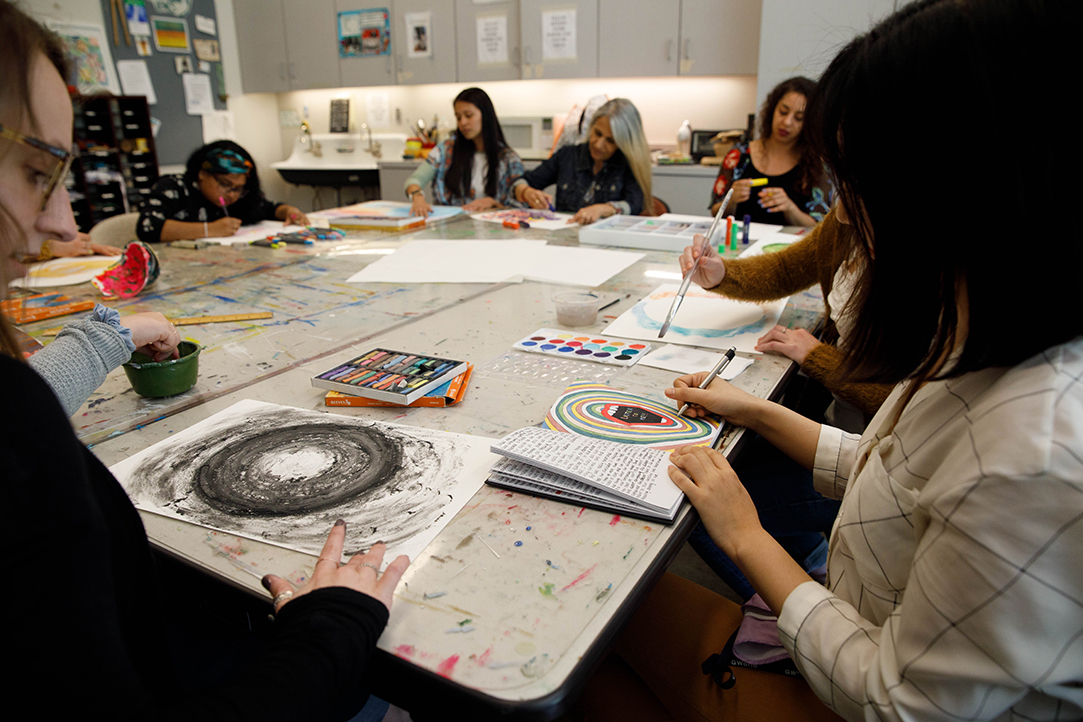 Close-up of two students and their artwork at a table of painting and drawing students.