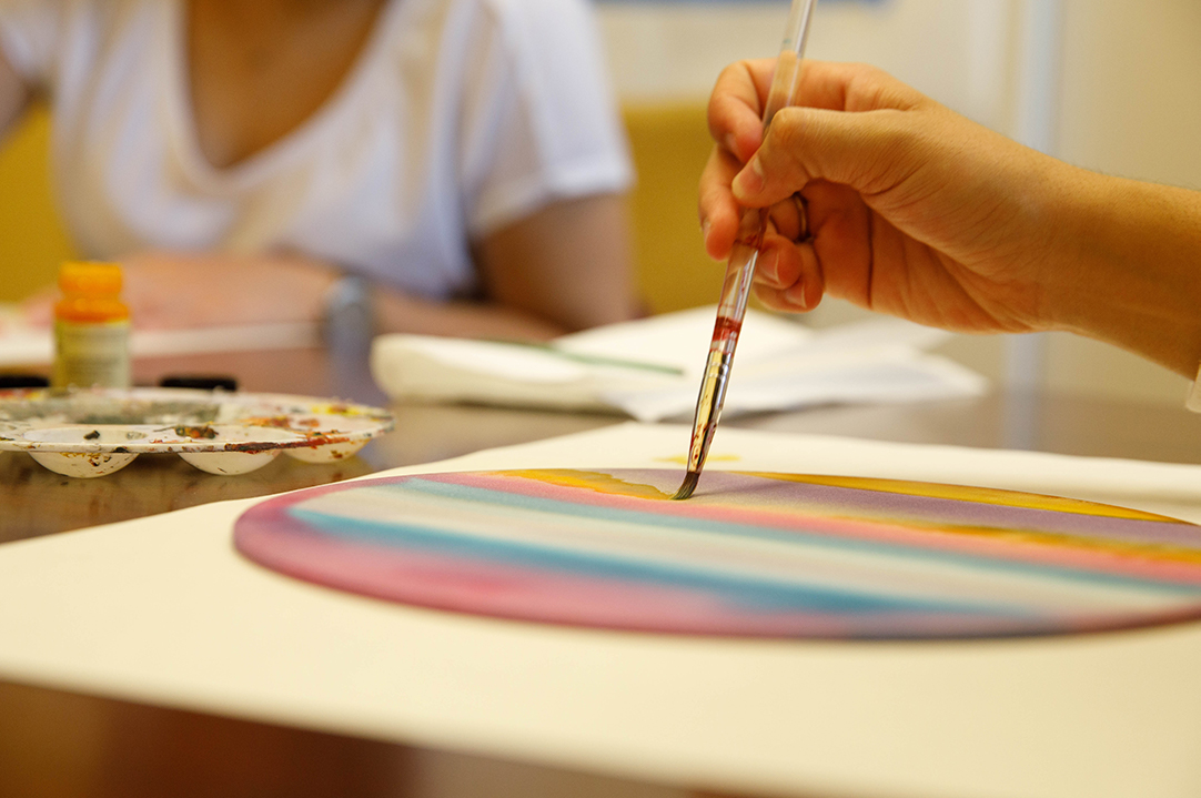 A person's hand holding a paintbrush and painting a colorful image