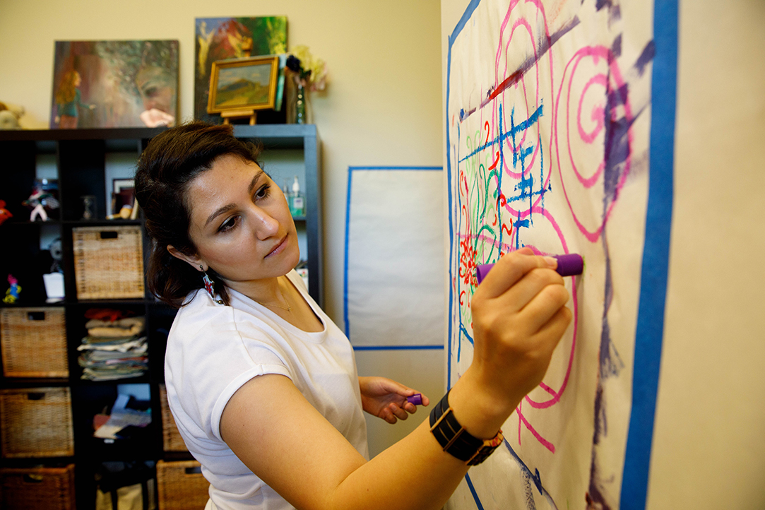 A female student draws with a purple marker on paper mounted to the wall in an office.