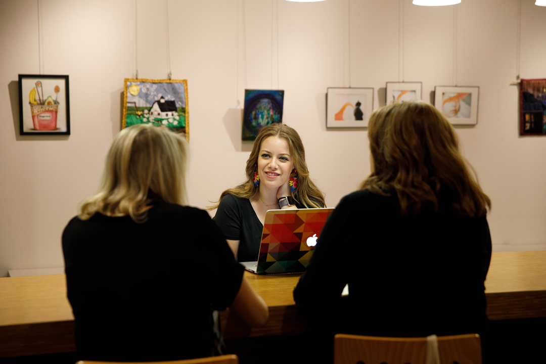 three art therapy students in conversation at a conference table surrounded by art