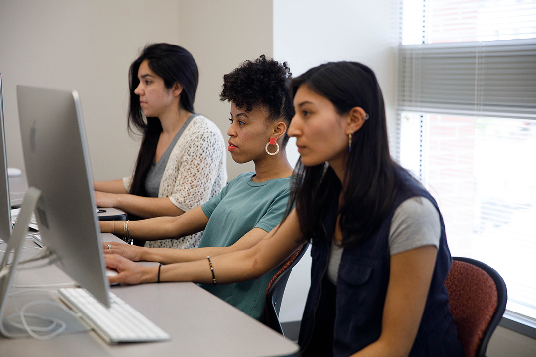Three female students sit in a row on computers.