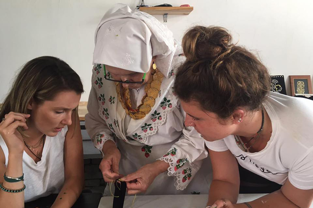 Two students learn embroidery from a Croatian woman.