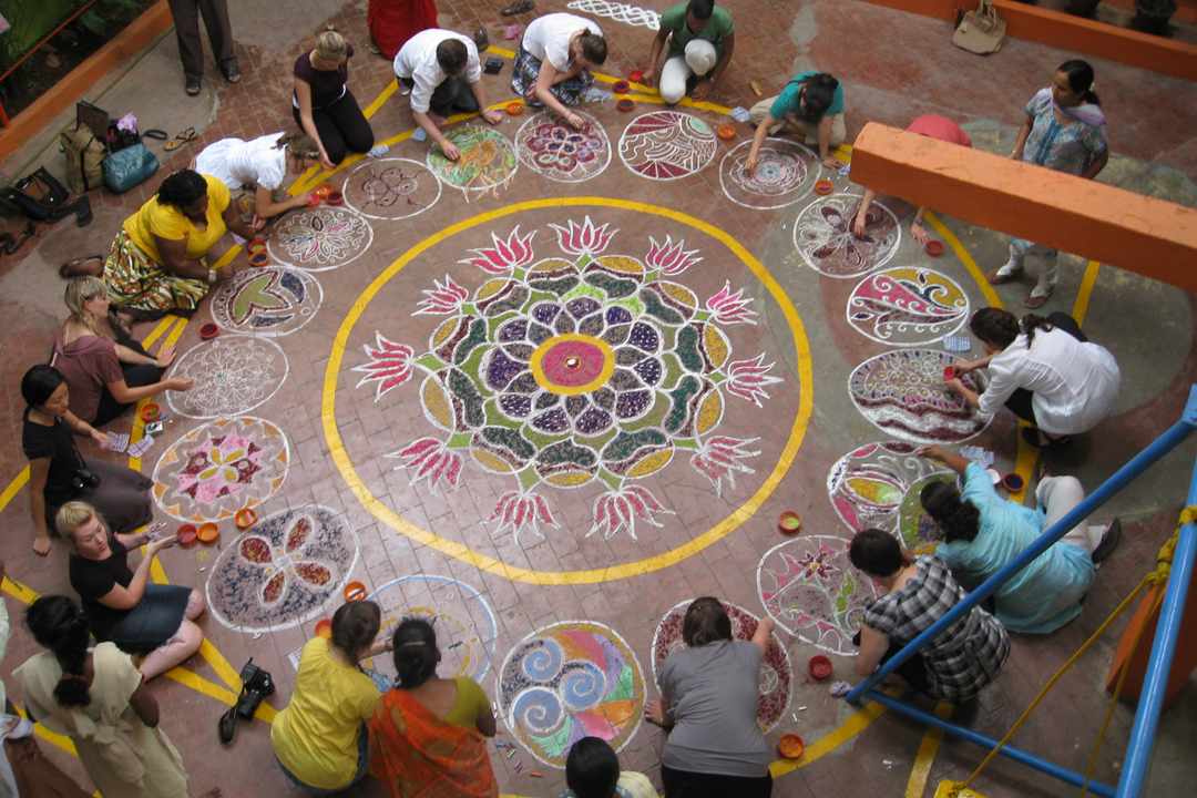 Program participants gathered together drawing a large mandala on a brick floor.