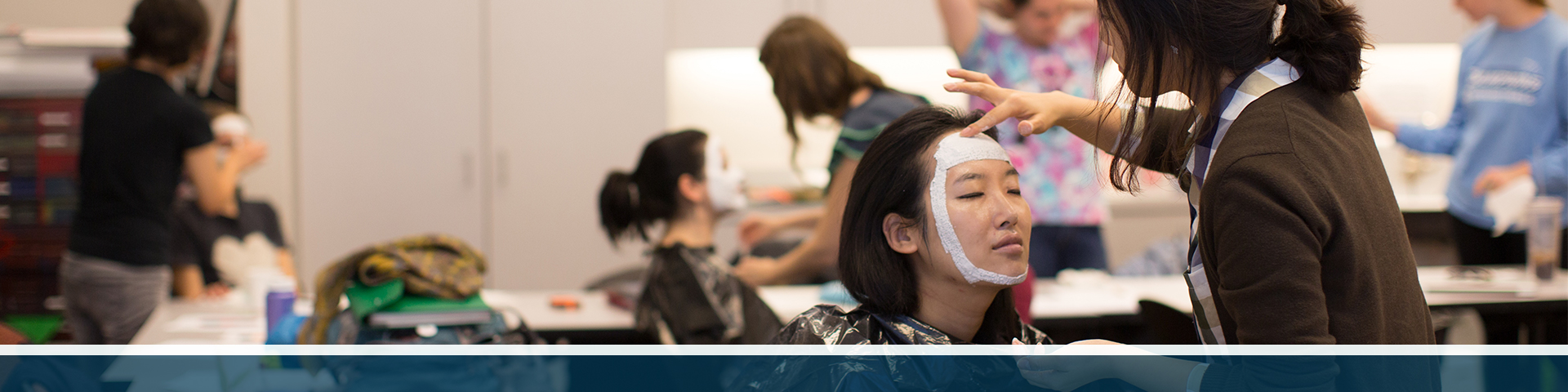 A student applies plaster to another student's face in order to make a mask.