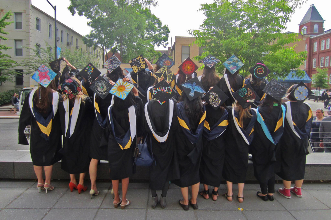 A group of graduates in their graduation caps and gowns showing the artwork on their caps.