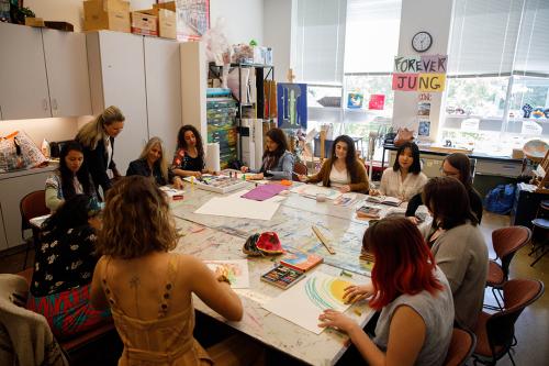 twelve students and professors seated at a large table drawing with pastels
